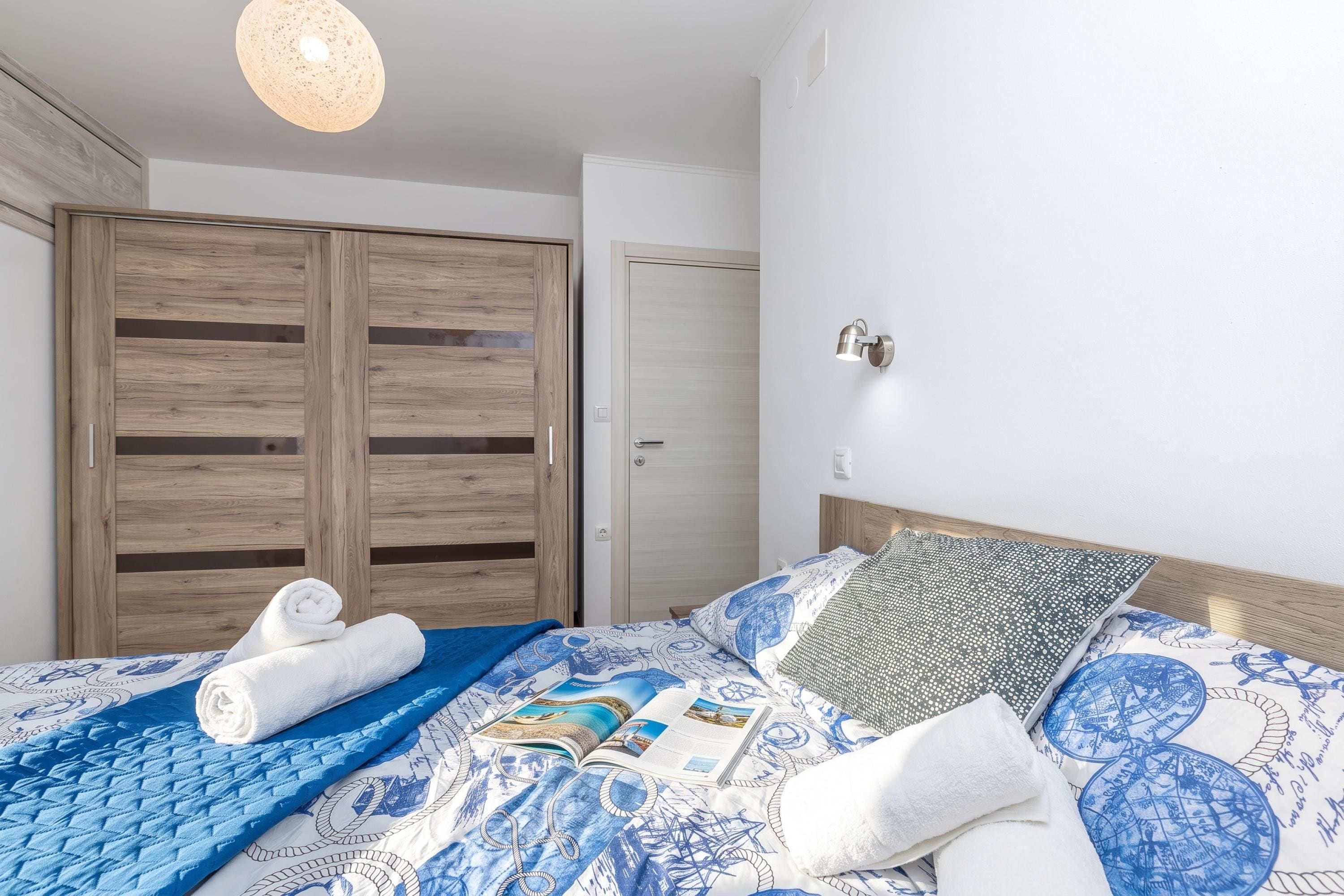 Un dormitorio con cama, armario de madera, una puerta y una lámpara fijada a la pared.