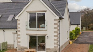 Une maison à deux étages dotée d’un patio comprenant une table en bois et des bancs.