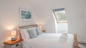 Une chambre à coucher avec un lit, une table de chevet, une lampe, une fenêtre et un tableau encadré au mur.