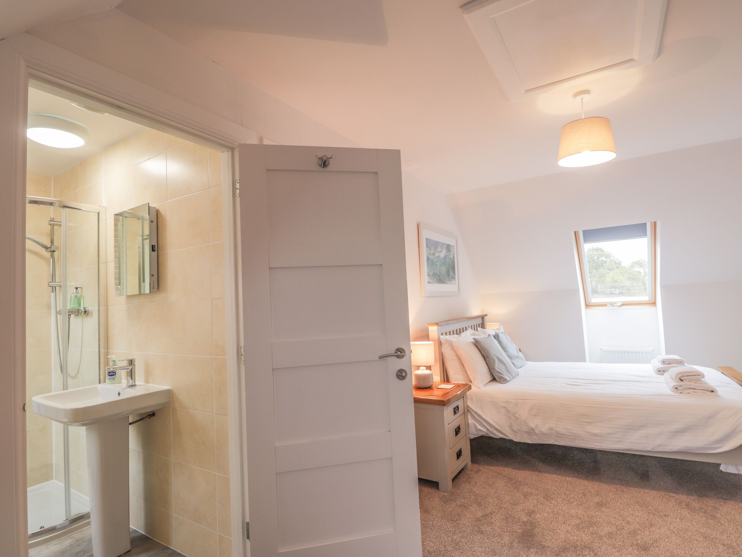 Un dormitorio con cama, mesita de noche, lámpara y ventana.