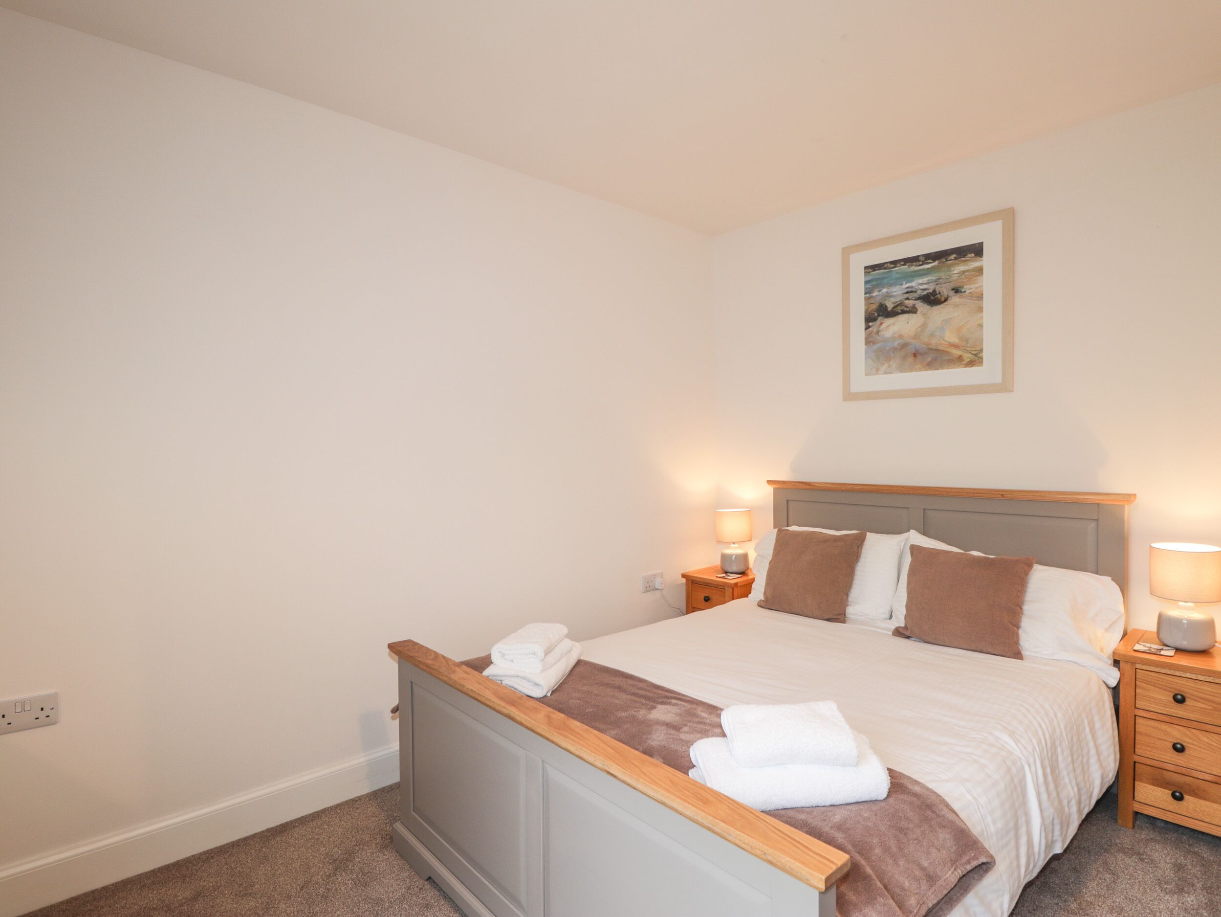 A neatly made bed with a wooden headboard, two bedside tables with lamps, and a painting on the wall.