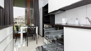 Una cocina moderna con armarios blancos, encimera negra y lavavajillas. Hay un comedor con mesa y sillas, y una ventana con cortinas.