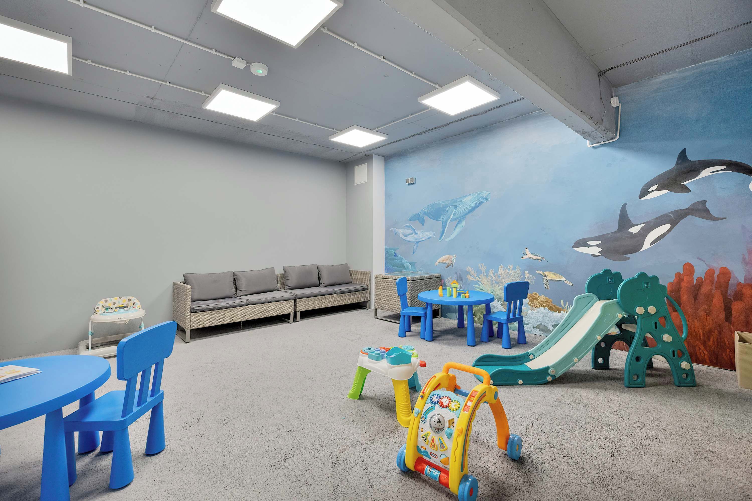A children's play area with a slide, a walker, and a mural of marine life.