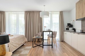 Une chambre d’hôtel moderne équipée d’un lit, d’une table à manger, de chaises, d’un coin cuisine et de grandes fenêtres avec des rideaux.