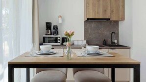 A modern kitchen with wooden cabinets, a microwave, a coffee maker, and a vase with flowers on the dining table. - Stylish Studio with Air Conditioning | Near the Beach | Parking (Mielno)