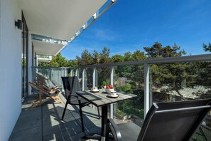 A balcony with a table and chairs, a glass railing, and a view of trees and buildings.