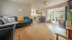 A modern living room with a black leather sofa, a woven rug, and a wooden dining table. - Castle Bungalow, Thornham, Norfolk (Thornham)