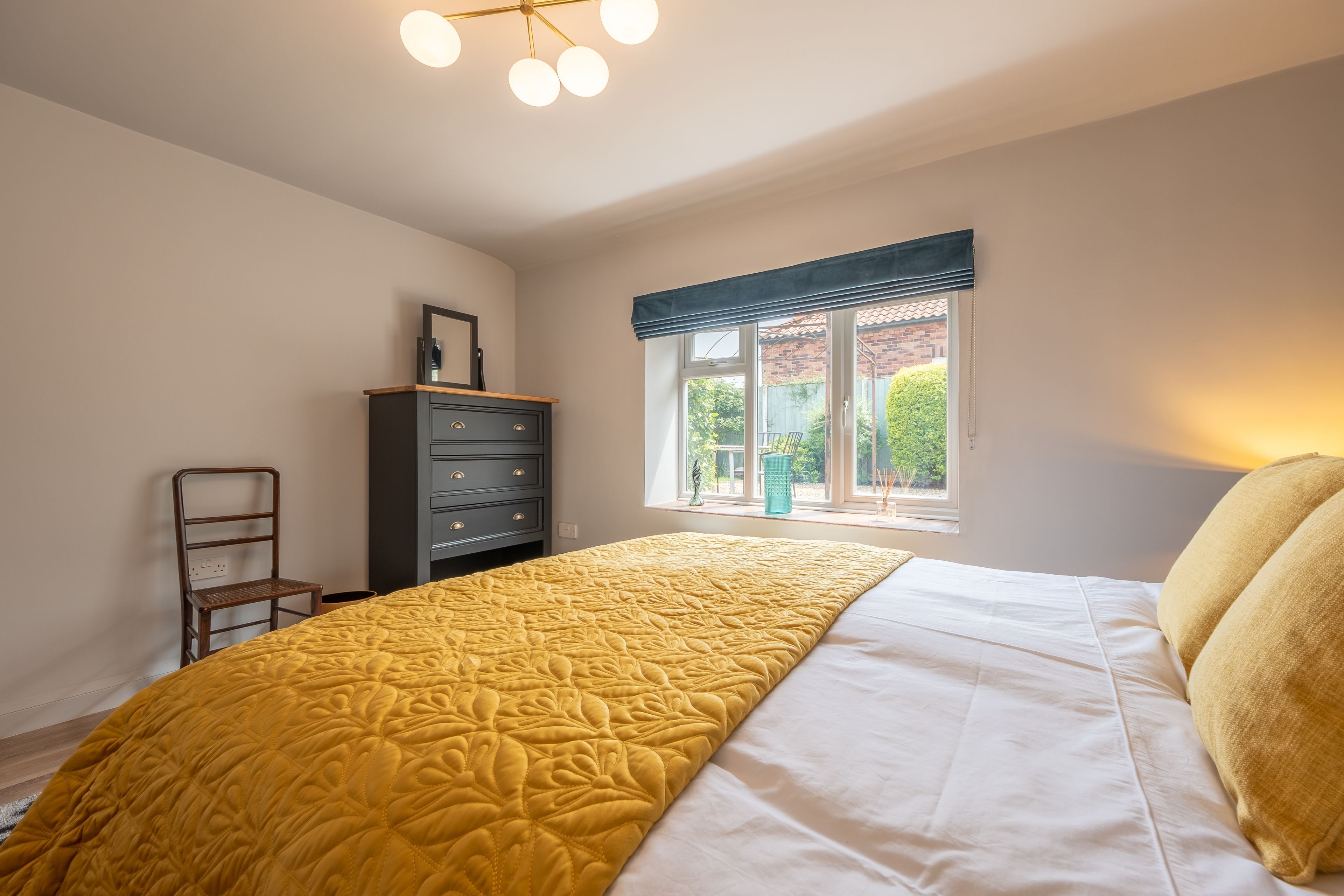 A bedroom with a bed, a dresser, a window with a view, and a ceiling light fixture.