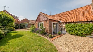 A residential property with a red-tiled roof, a well-maintained lawn, and a gravel driveway. - Castle Bungalow, Thornham, Norfolk (Thornham)
