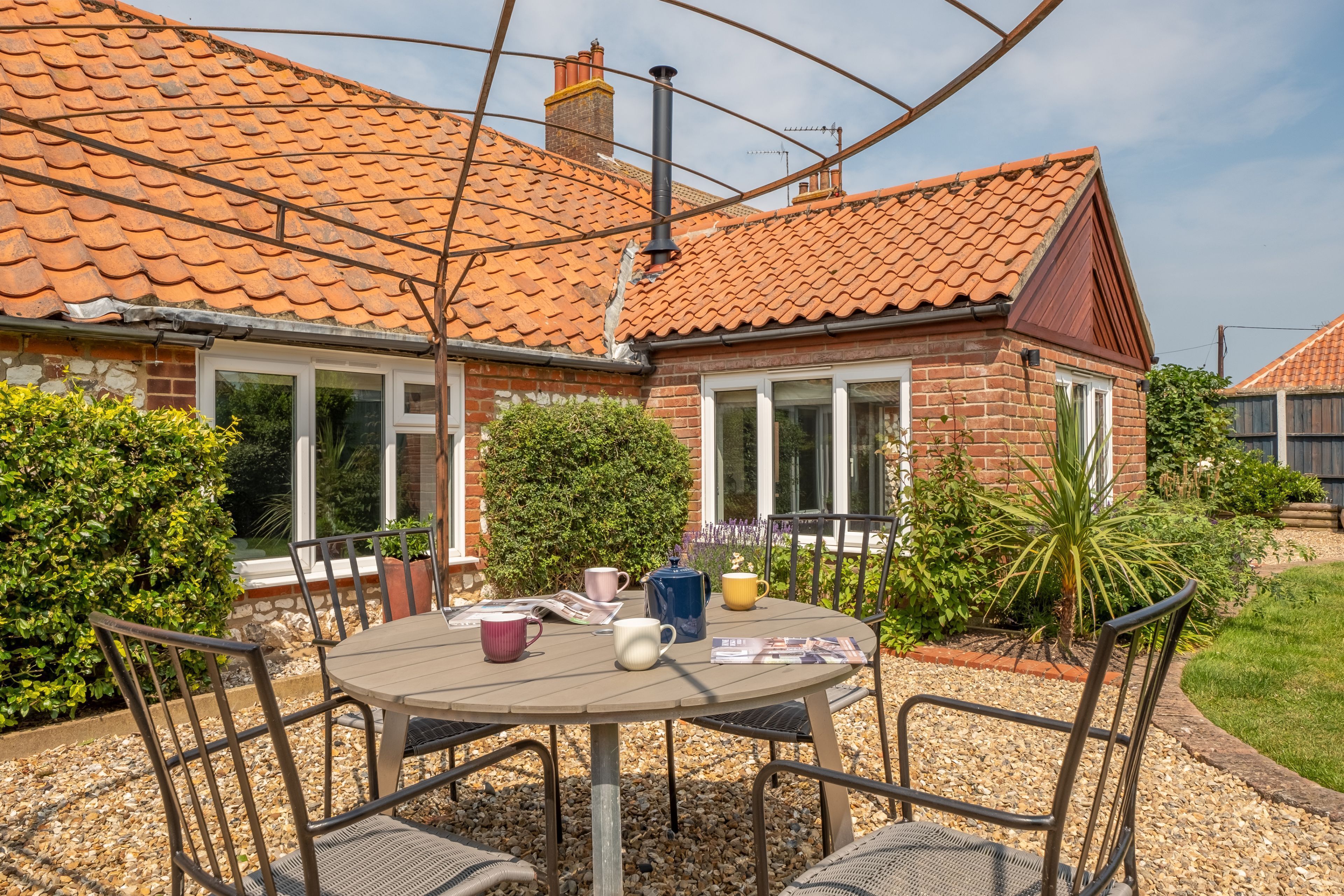 A house with a tiled roof, brick walls, and a garden with a table and chairs.