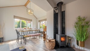 A modern living room with a fireplace, wooden flooring, a dining area with a table and chairs, and large windows. - Castle Bungalow, Thornham, Norfolk (Thornham)