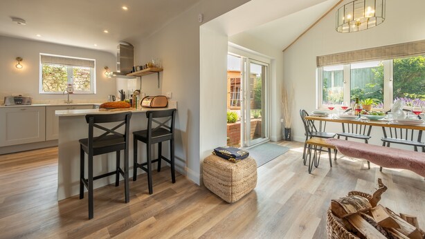A spacious kitchen with a central island, wooden flooring, and a dining area with a table set for four. - Castle Bungalow, Thornham, Norfolk (Thornham)