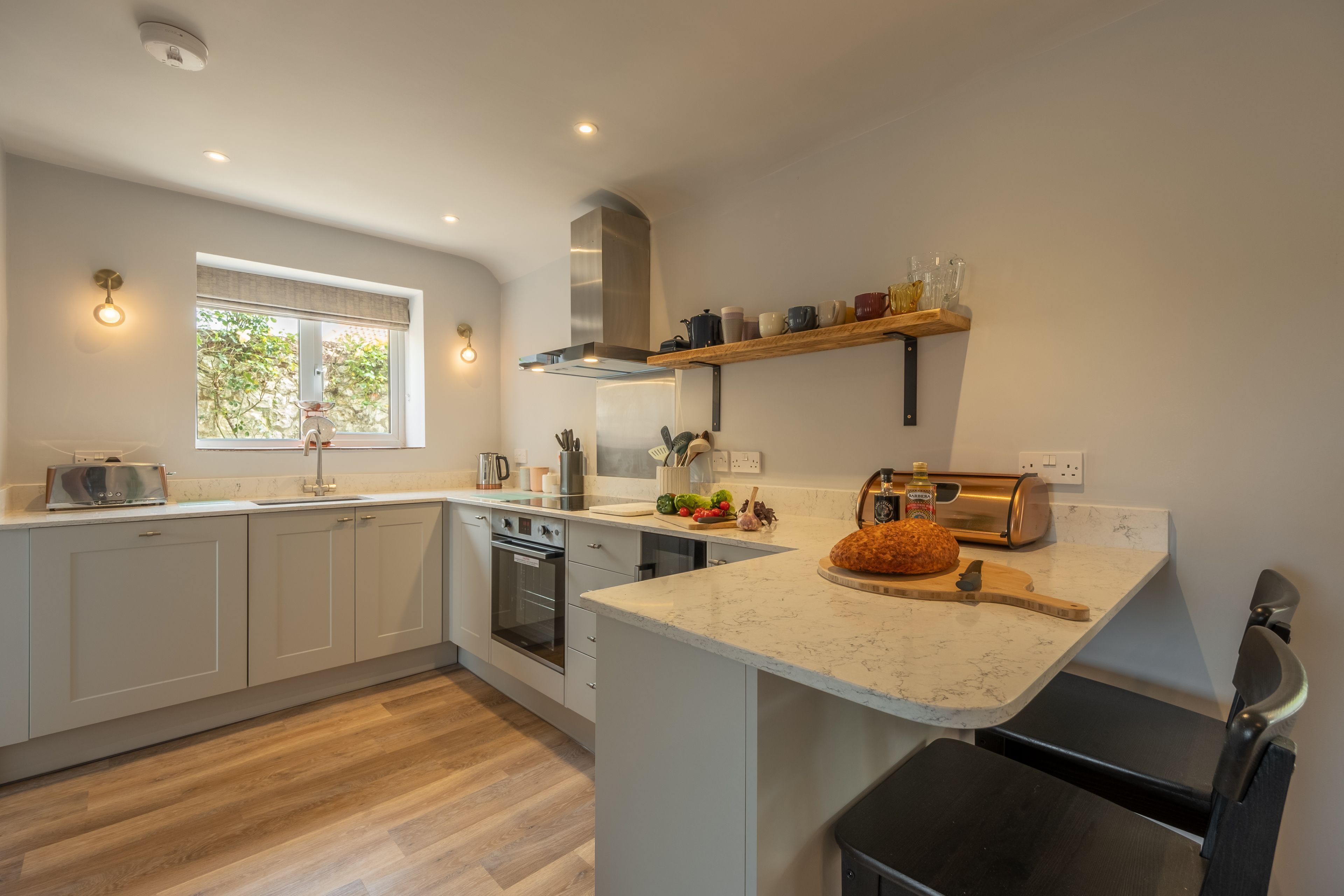A modern kitchen with white cabinetry, a built-in oven, and a window with a view of greenery.