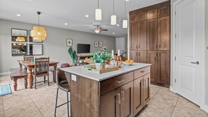 Una cocina moderna con una isla central, armarios de madera, iluminación colgante y una zona de comedor con mesa y sillas.