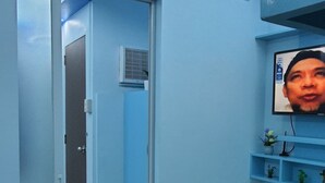 A hotel room with a wooden floor, a glass door leading to a hallway, a mounted air conditioner, and a wall-mounted TV. - Mistow BriaCondo City Center Area (Cagayan de Oro)