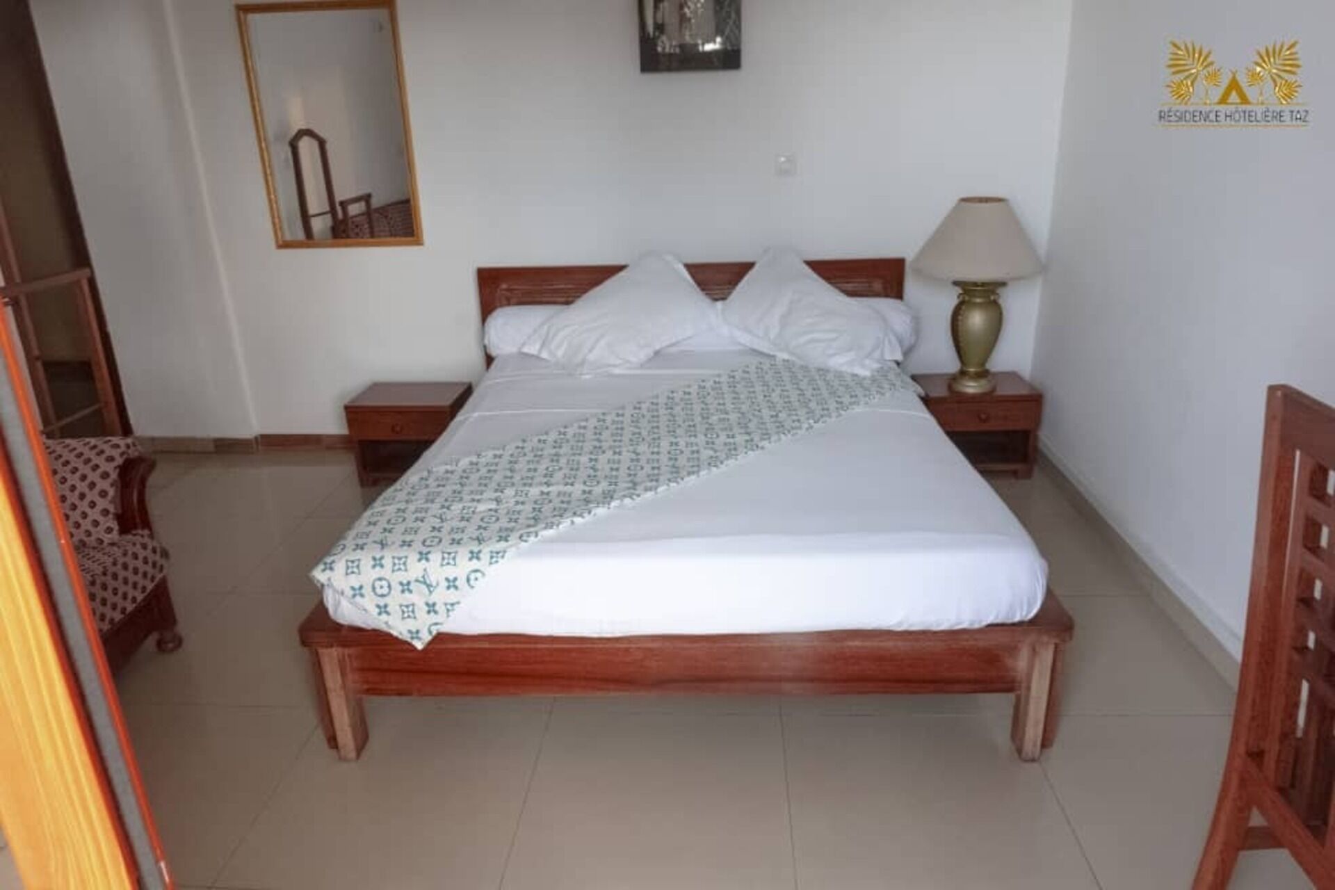 A neatly made bed with a patterned bedspread, a bedside lamp, and a nightstand with a small drawer.