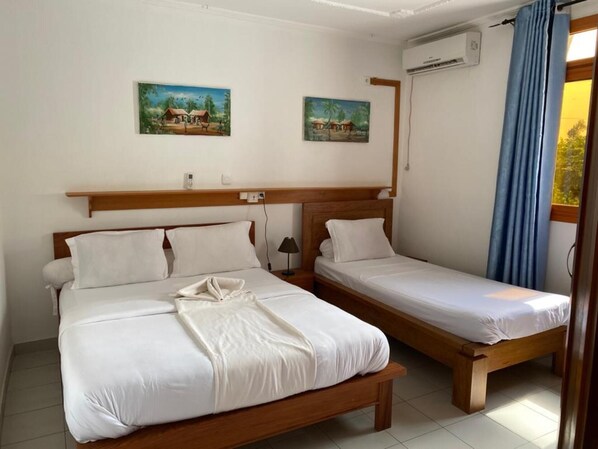 A hotel room with two beds, a wooden headboard, a small table, and two paintings on the wall.