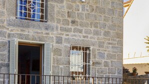 A stone building with a swimming pool, a balcony with a railing, and a window with shutters.