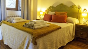A neatly made bed with folded towels and a blanket, a nightstand with a lamp, and a window with curtains.
