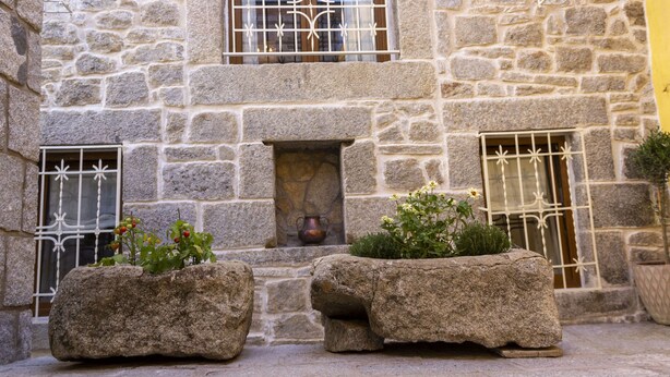 A stone building with a small window and a door, a stone bench, and a potted plant.