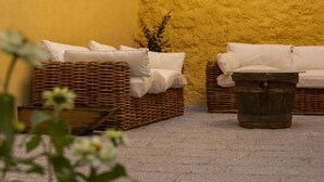 Two wicker sofas with white cushions against a yellow wall, a rustic wooden bucket, and a small plant.