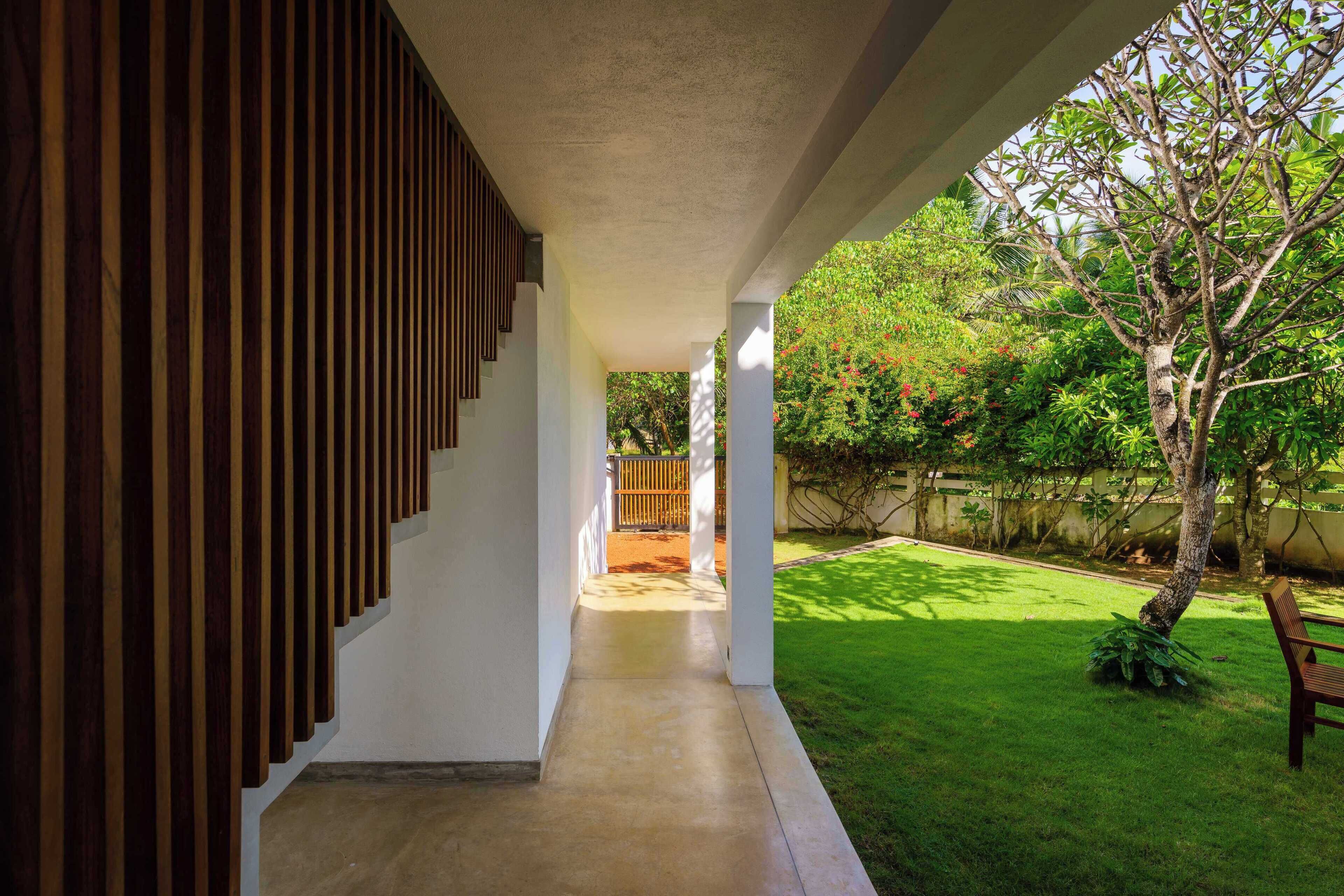 Un corredor exterior cubierto con una pared de listones de madera en un lado, que conduce a un área con césped, un árbol y un banco.