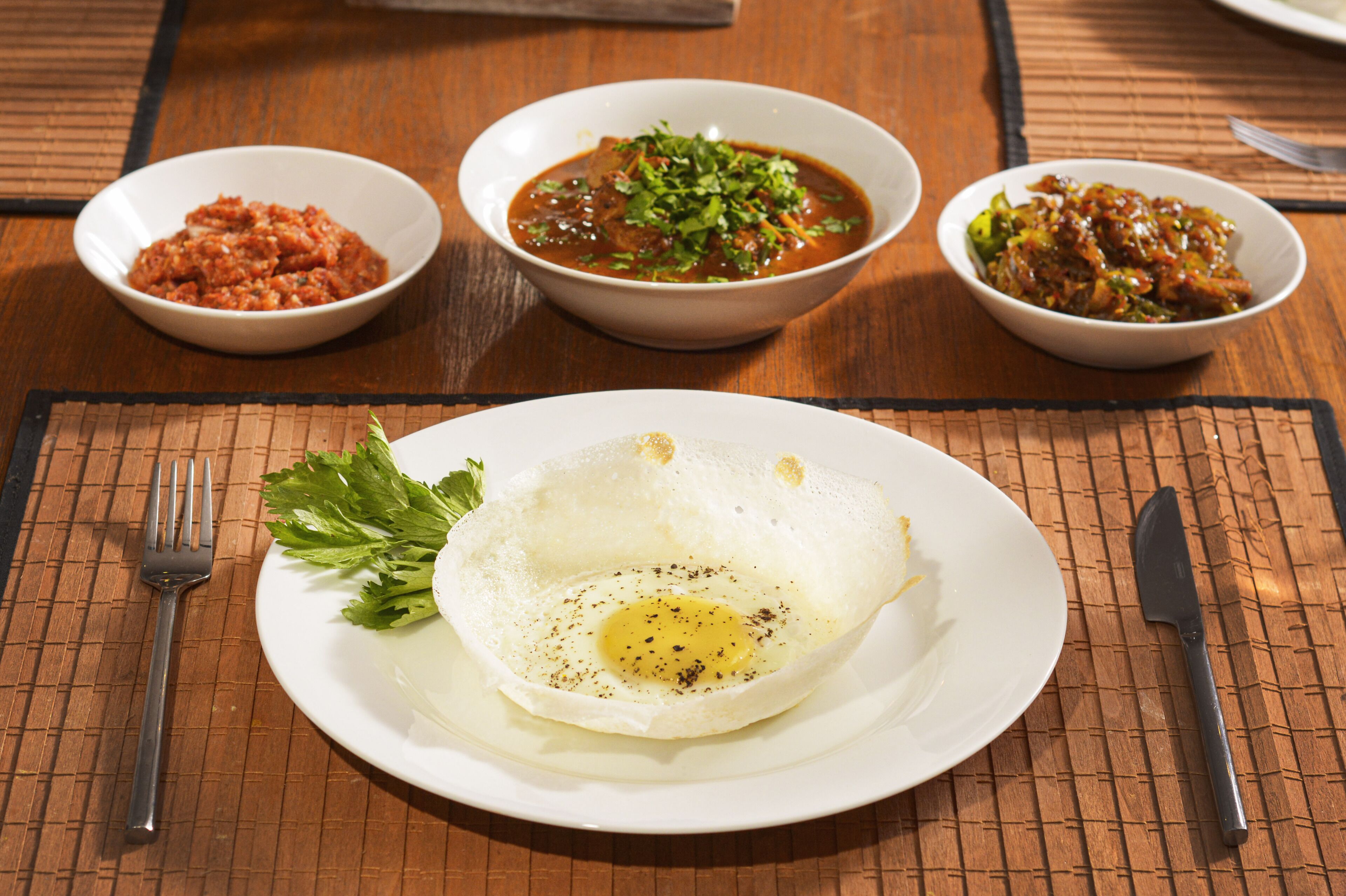 A table with a plate of fried egg, three bowls of side dishes, and cutlery.
