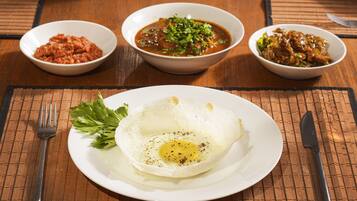 A table with a plate of fried egg, three bowls of side dishes, and cutlery.