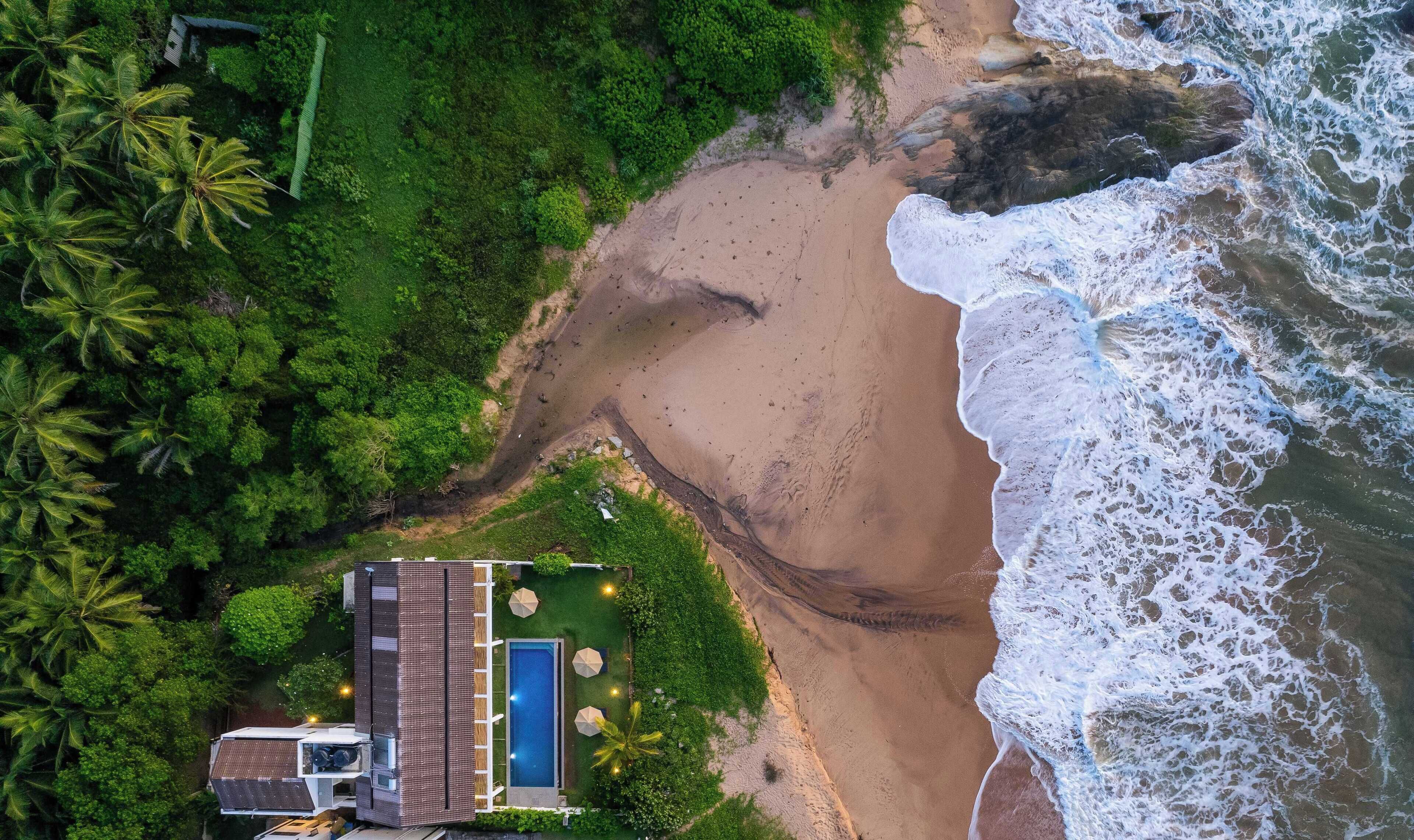An aerial view of a beach with a small building and a pool.