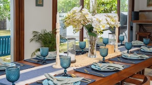 A dining table set with blue glassware, plates, and napkins, with a vase of white flowers in the center. - Villa Tanderra (Kalametiya)