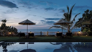 A poolside area with two umbrellas, lounge chairs, and a wooden fence overlooking the ocean. - Villa Tanderra (Kalametiya)