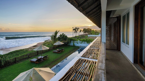 A balcony with a view of the ocean, a pool, and a grassy area with umbrellas. - Villa Tanderra (Kalametiya)