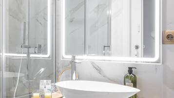 A modern bathroom with a glass shower enclosure, a white marble sink, and a large mirror with integrated lighting.