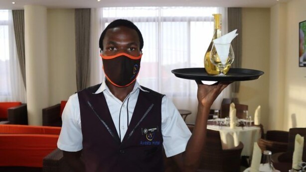 A hotel staff member holding a tray with a bottle and a folded napkin. - Avesta Hotel (Kampala)