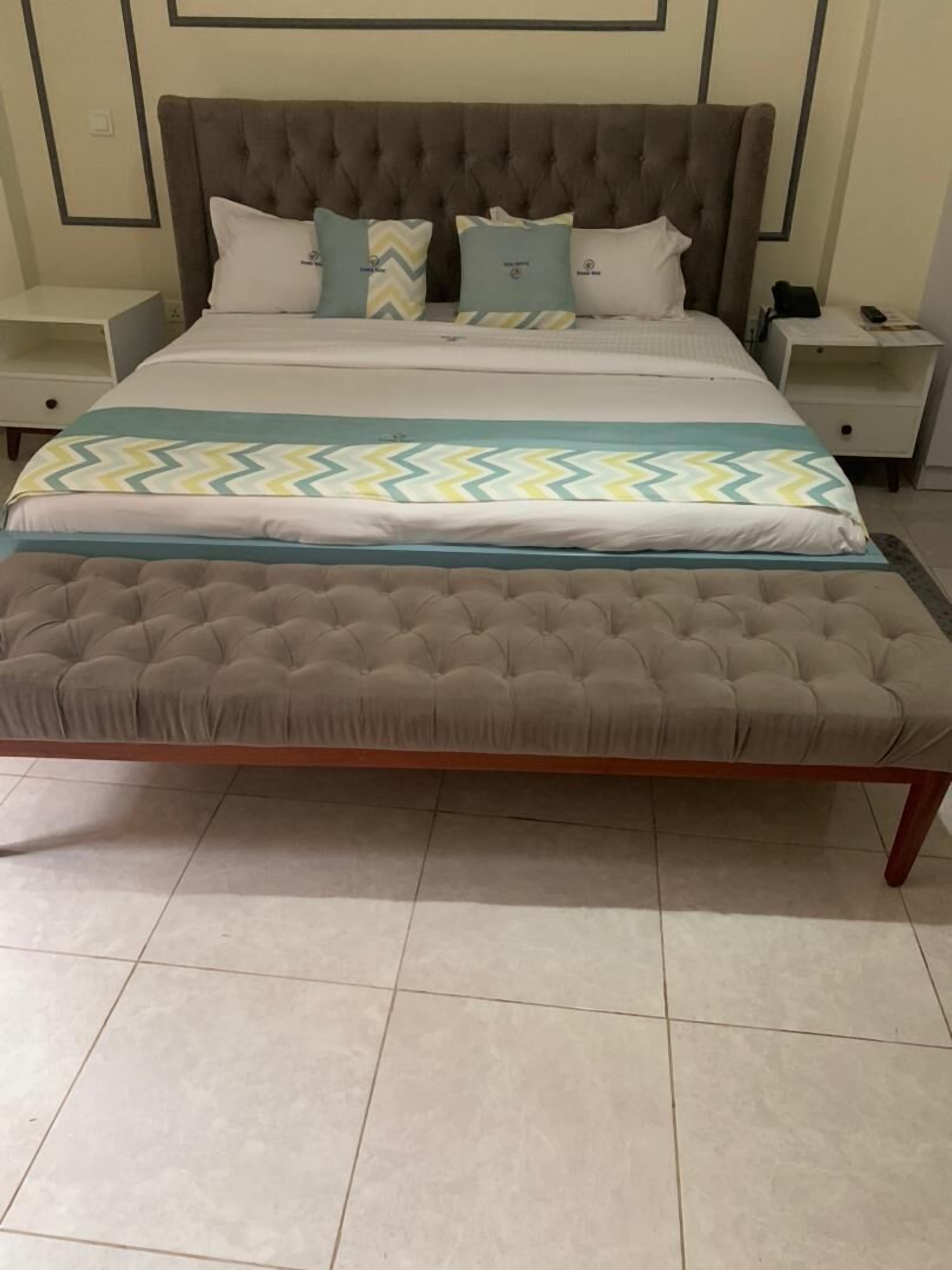 Un lit doté d’une tête de lit capitonnée, d’un banc assorti et d’une couvre-lit à motifs.