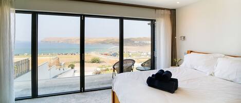 A bedroom with a large sliding glass door leading to a balcony with a view of the sea and hills.