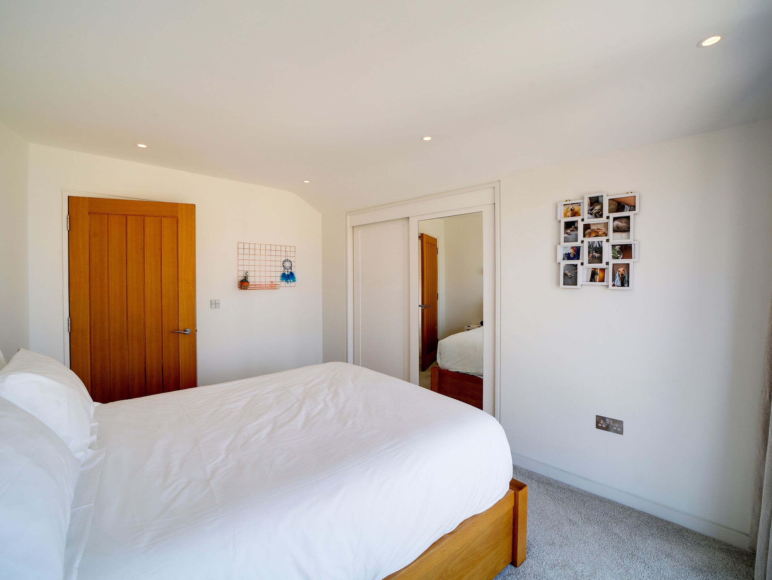 A bedroom with a wooden bed, a wardrobe, a mirror, and a wall with photos.