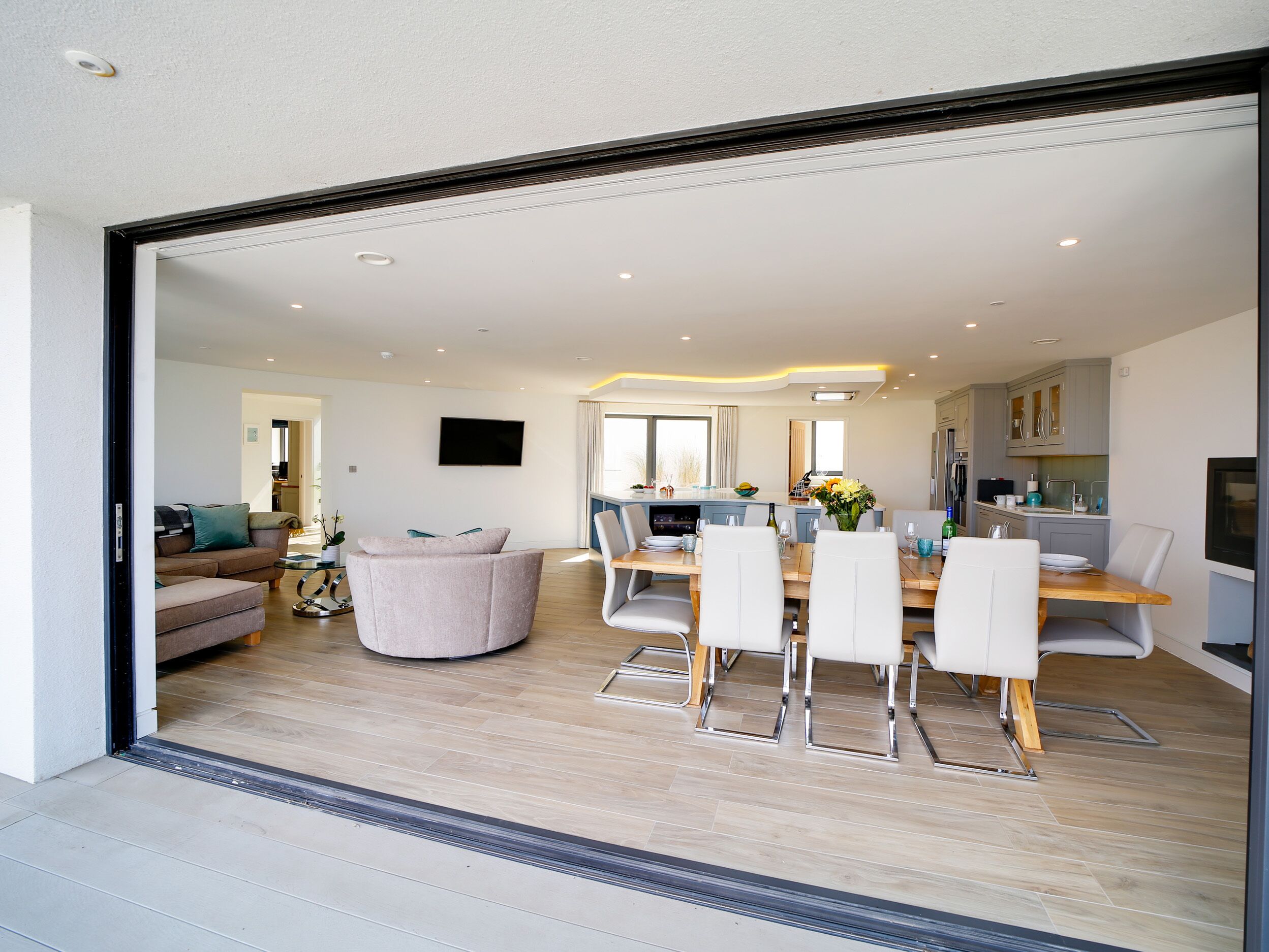 A modern kitchen with a dining area, a flat-screen TV, and a sofa in the living room.