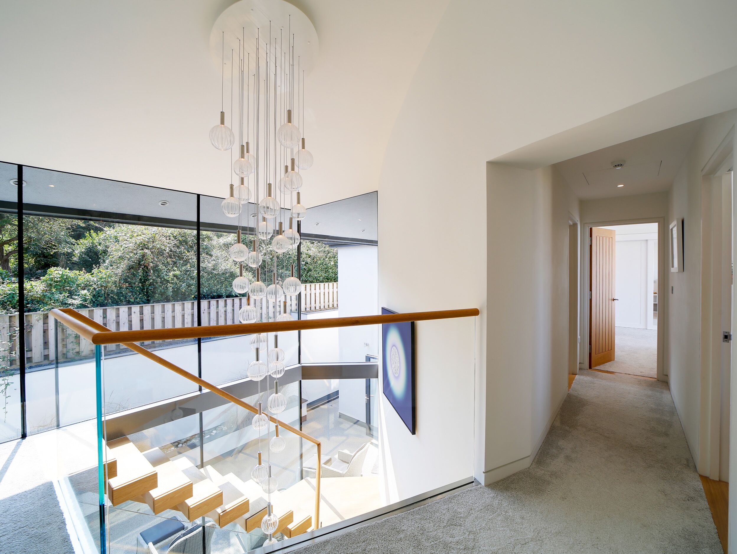 A modern interior with a glass staircase, a hanging light fixture, and a view of greenery outside.