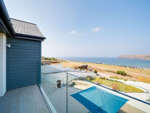 Un balcón con vista al mar, una piscina y un edificio moderno con techo inclinado.
