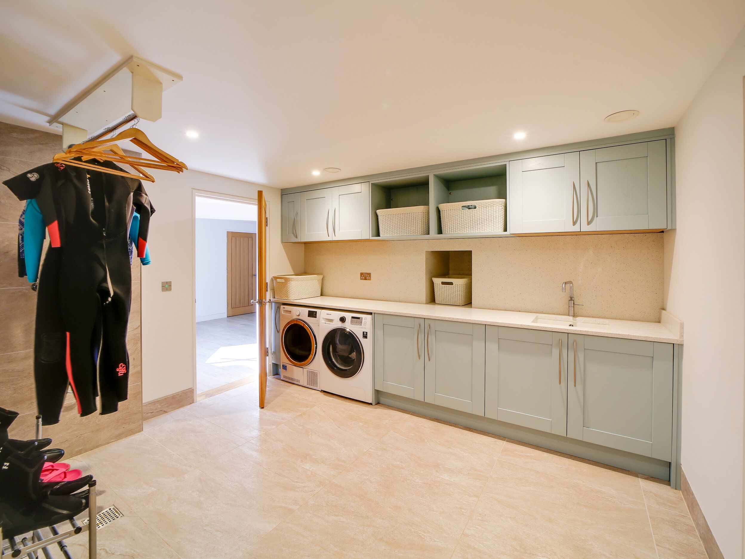 A laundry area with a washing machine and drying rack, a kitchenette with a sink and cabinets, and a hallway with a door leading to another room.