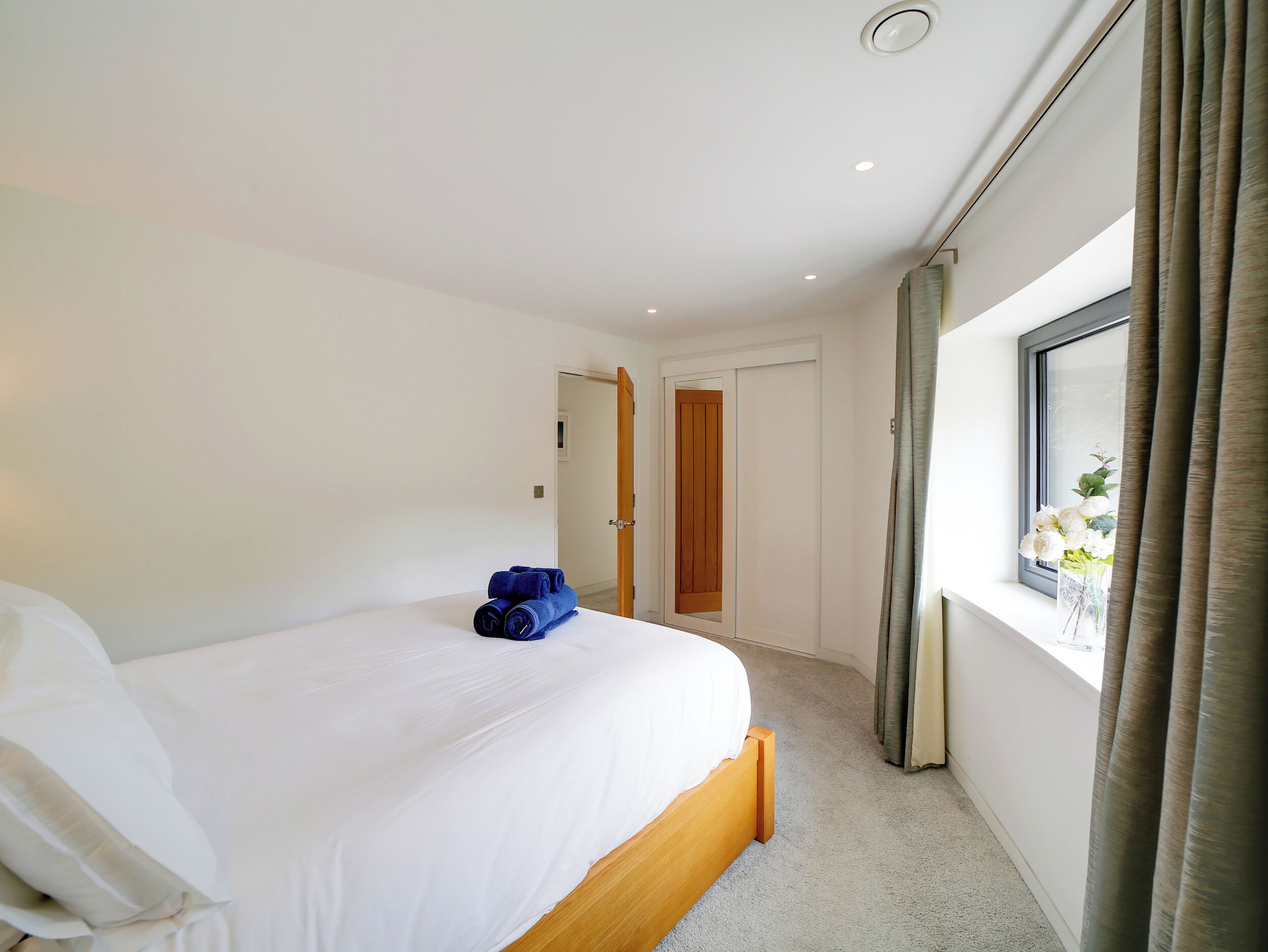 A hotel room with a bed, a wooden headboard, a window with curtains, and a door leading to another room.