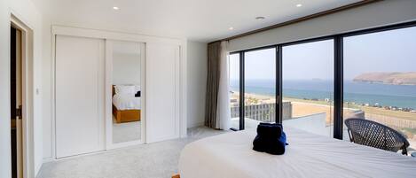 A modern hotel room with a large bed, a view of the beach, and a balcony with a chair.