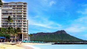 A beachfront hotel with multiple balconies, a sandy beach, and a mountain in the background. - LUXURY DIRECT OCEANFRONT! Fully Renovated! Free Parking! Sleeps 6 (Honolulu)