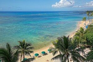 A beach with clear turquoise water, palm trees, and beach umbrellas.