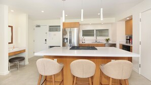 A modern kitchen with a large island, stainless steel appliances, and three bar stools.