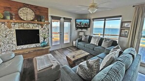 A living room with a large window, a flat-screen TV, and a ceiling fan. - Beach House on the Bay - Fisherman's Paradise on the bay! (Port Bolivar)