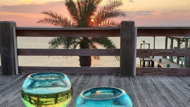 Two glass vases on a wooden deck with a view of the sunset and palm trees. - Beach House on the Bay - Fisherman's Paradise on the bay! (Port Bolivar)