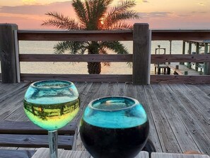 Two glass vases on a wooden deck with a view of the sunset and palm trees. - Beach House on the Bay - Fisherman's Paradise on the bay! (Port Bolivar)