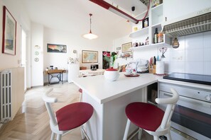 A modern kitchen with a central island, white bar stools, and a built-in oven. - Between the Sea and the Hills (Monteprandone)